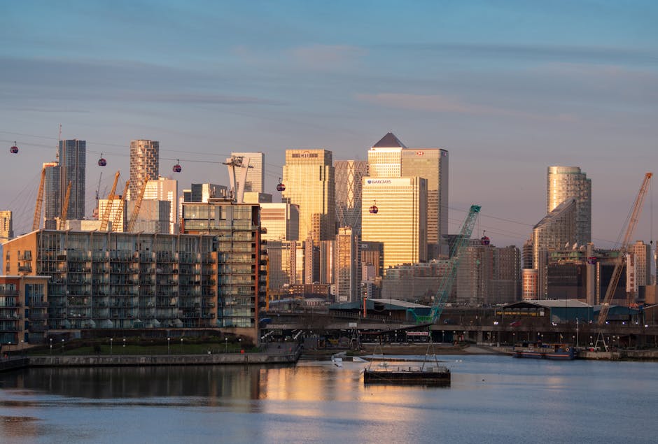 A view of modern high-rise office buildings in a commercial district, with reflective glass facades and a partly cloudy sky overhead. In the foreground, a narrow canal runs alongside the buildings wit